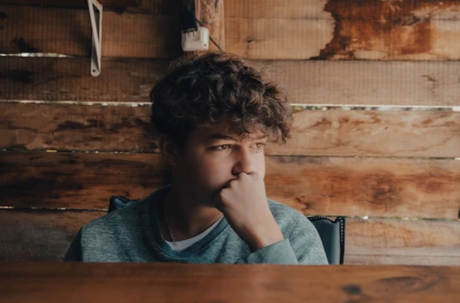 Nervous teen covering mouth with hand looking out in front of wooden background